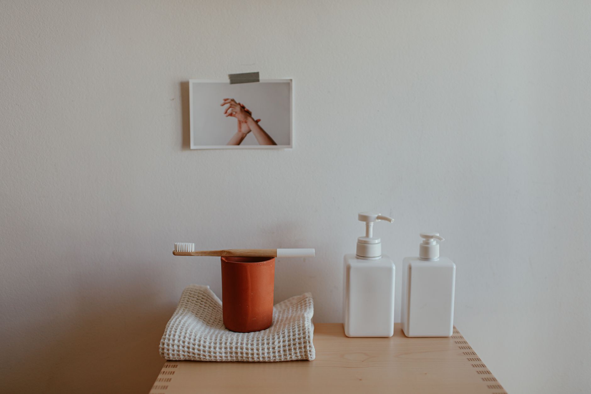Minimalist bathroom setup with toothbrush, cup, and soap dispensers on wooden dresser.