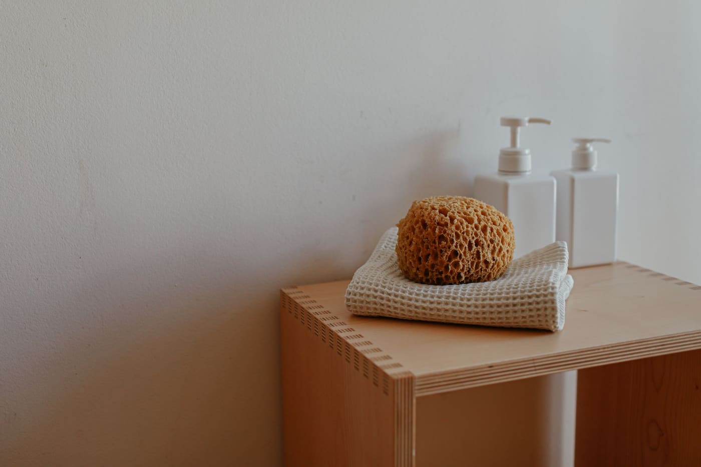 Folded towel with a natural sponge and two pump bottles on a small wooden shelf
