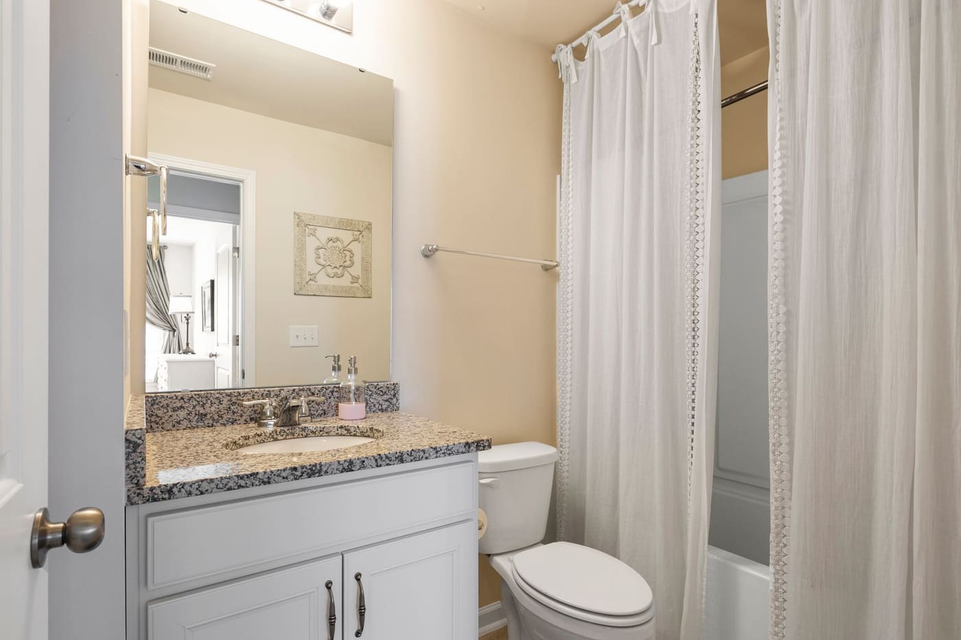 White fabric shower curtain beside a vanity with a granite countertop