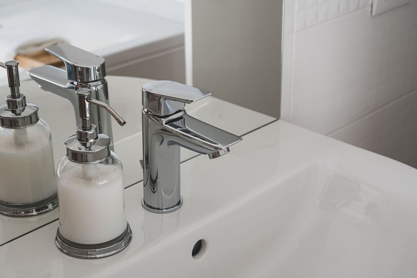 Chrome faucet and soap dispenser on a clean white bathroom sink