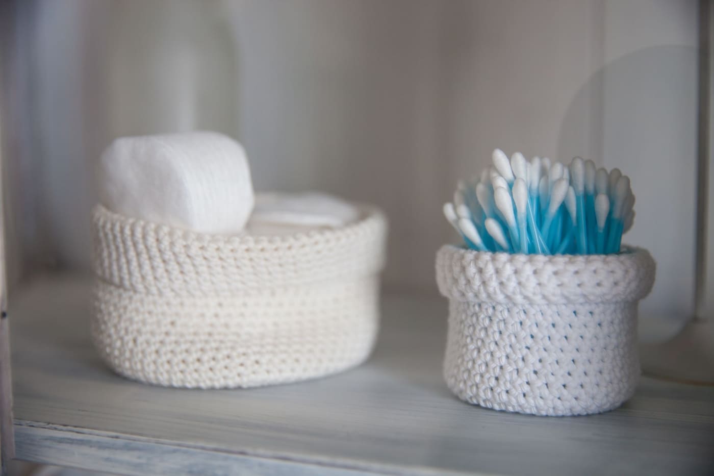 Two small crocheted baskets holding cotton pads and swabs