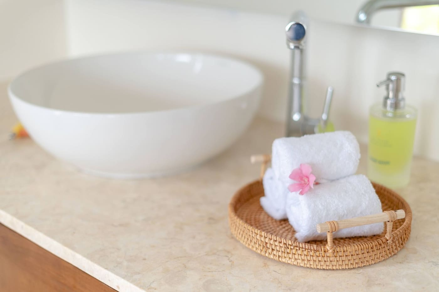 Rolled hand towels and a soap dispenser on a woven tray beside a bowl sink