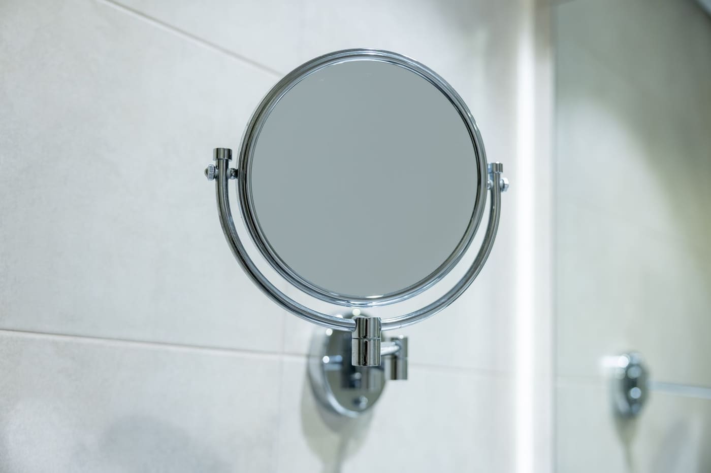 Round two-sided chrome mirror mounted on a tiled wall