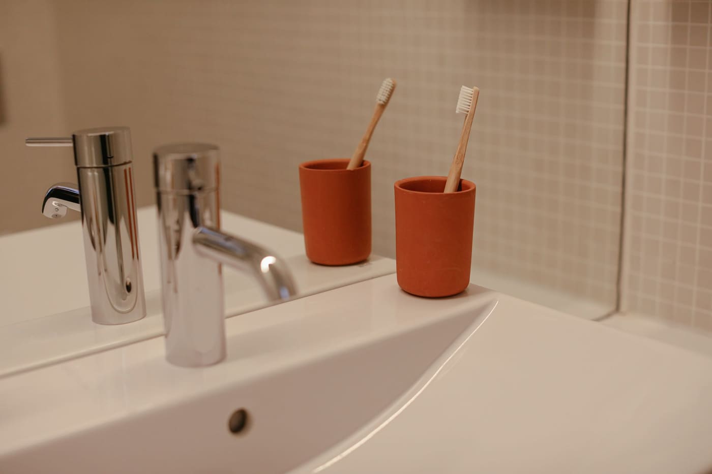 Two orange cups holding toothbrushes beside a bathroom sink faucet