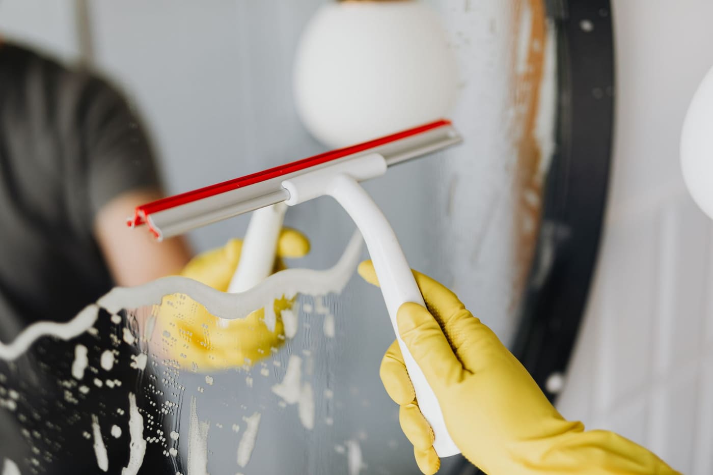 Gloved hand pulling a squeegee across a wet glass surface