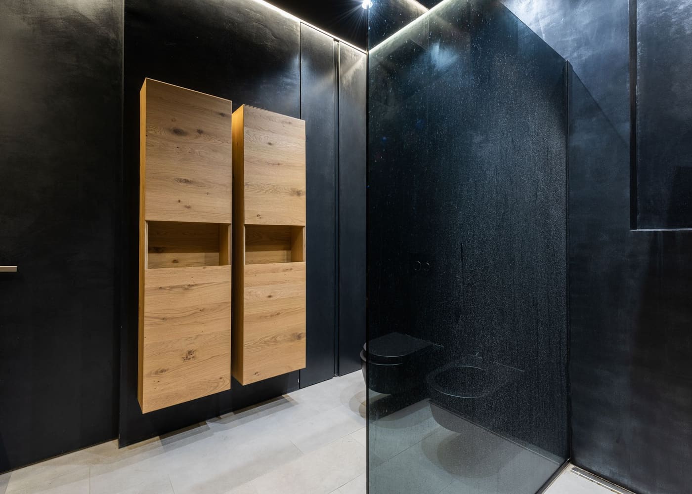 Two narrow wooden wall cupboards on a dark bathroom wall