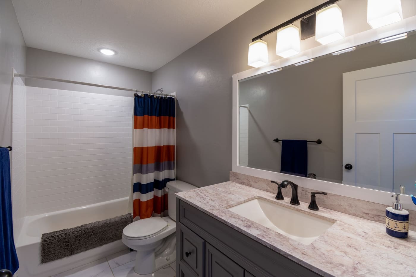 Bathroom vanity with a three-bulb light bar over the mirror and a striped shower curtain