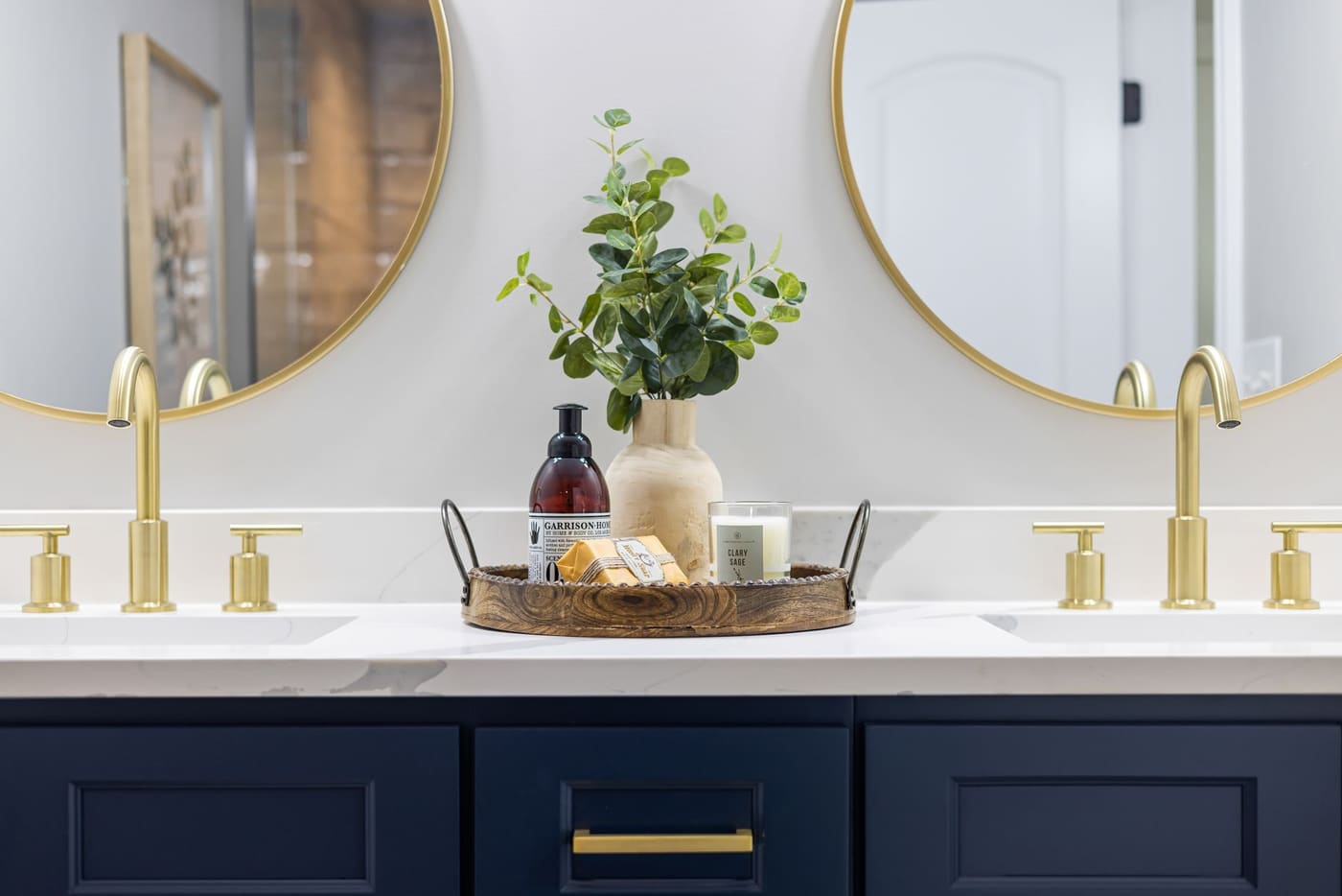 Double vanity with a small tray on the counter between two gold faucets
