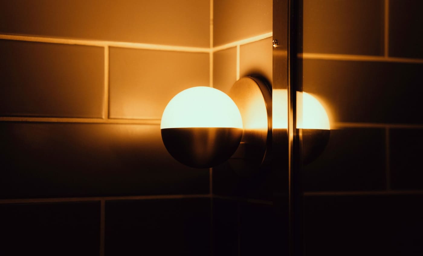 Warm globe wall light glowing against a tiled wall