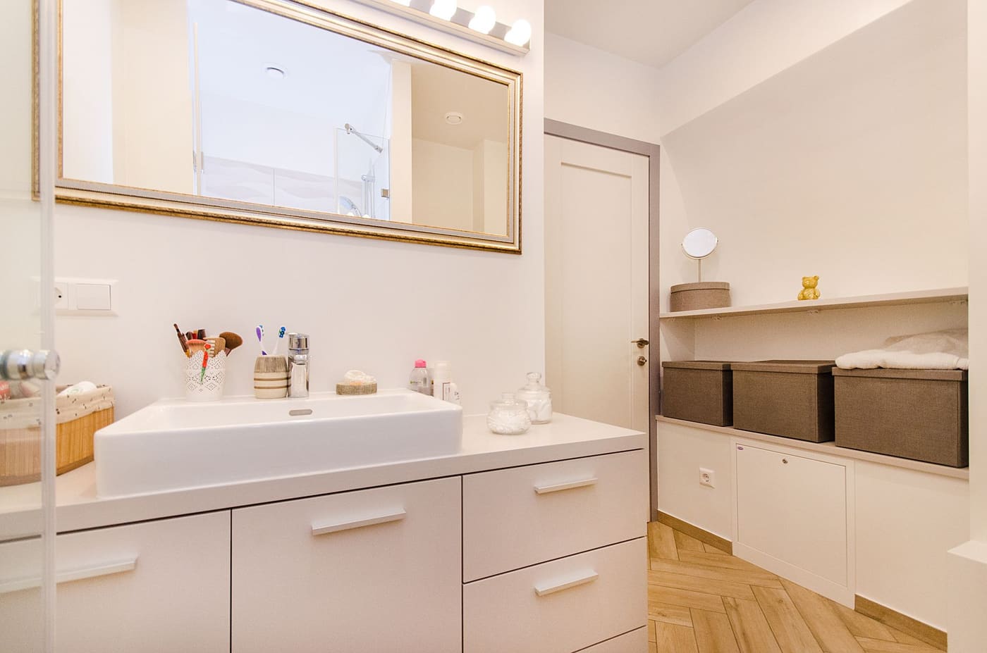 White bathroom vanity with dark fabric bins on an open shelf beside it